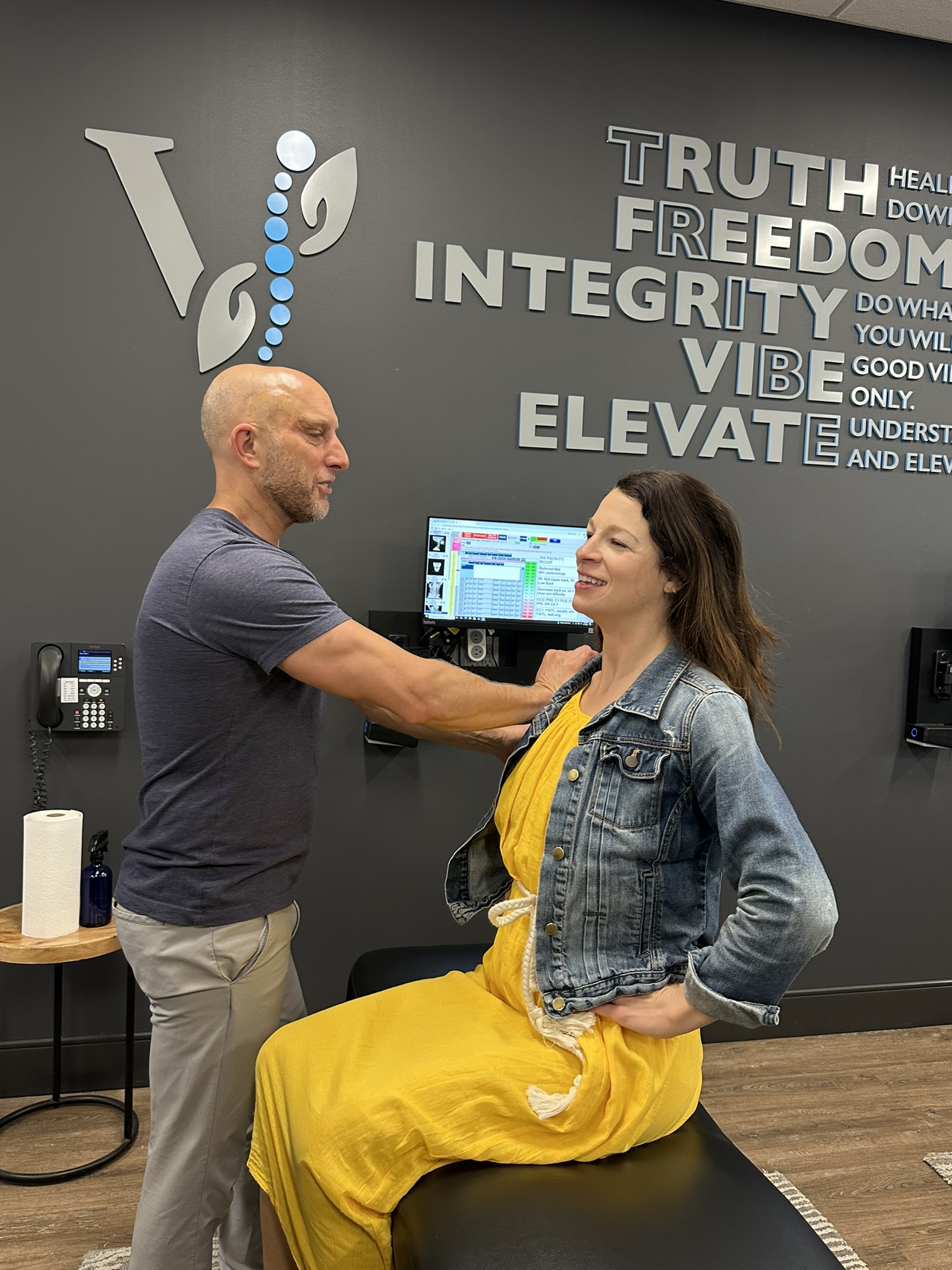 Fishers, IN chiropractor performing a posture and shoulder-height assessment for scoliosis screening in a modern clinic room