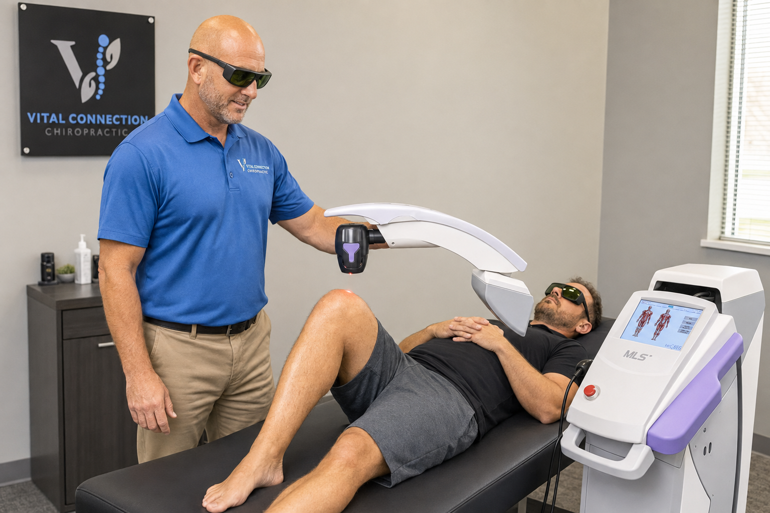 Dr. Jared Himsel supervises Robotic M7 MLS laser therapy for an adult patient’s knee while both wear protective eyewear., deep tissue laser therapy, deep tissue laser treatment, laser muscle therapy, therapeutic laser,